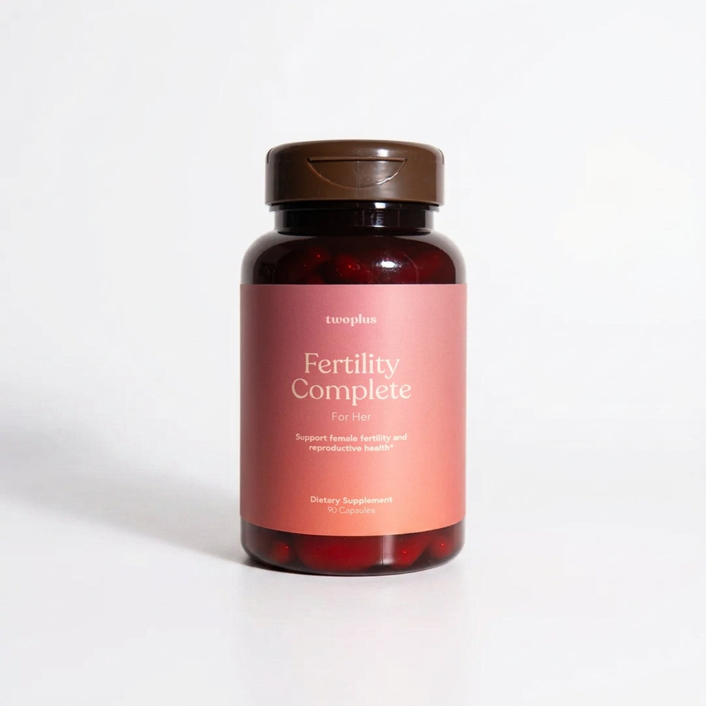 A bottle of 'Fertility Complete for Her' supplements by twoplus Fertility, with a pink label on a white background.