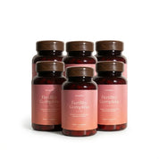 Six bottles of 'Fertility Complete for Her' supplement on a white background